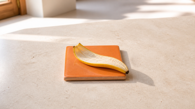 A strip of ripe banana peel, inner side up, on an orange ceramic tile on pale stone