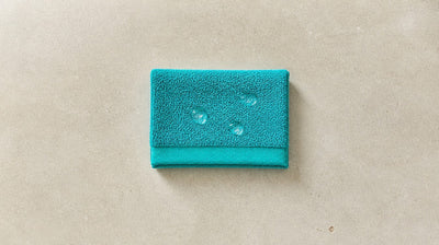 Clear serum splashes on a folded teal terry towel with no bleach marks, showing salicylic acid does not bleach fabric
