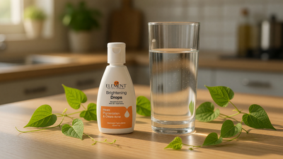 Giloy (Tinospora cordifolia) heart-shaped leaves beside The Element Brightening Drops (30ml) and a taller glass of water on a kitchen counter