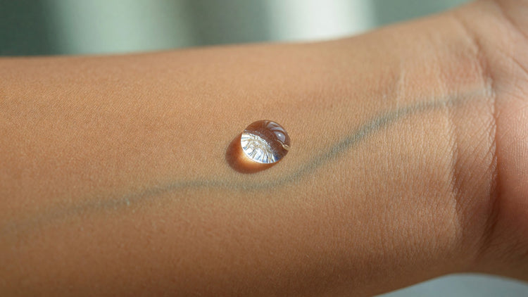Close-up of a small clear bead of serum patch-tested on the smooth inner forearm of warm brown Indian skin