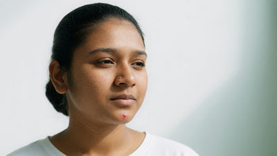 Young Indian woman with warm brown skin and a small pimple on her chin, hands away from her face, resisting the urge to squeeze it