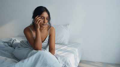 Indian woman with warm brown skin waking up tired in bed in soft morning light, with visible under-eye shadows
