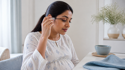 Pregnant Indian woman applying a slim lash serum wand to her upper lashes at a bright vanity