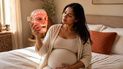 Pregnant Indian woman examining a glowing red LED light-therapy face mask before deciding whether to use it