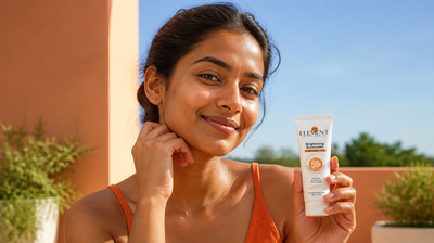 Indian woman with deep warm-brown skin on a sunlit balcony holding The Element 2% Niacinamide Brightening Sunscreen, no white cast on her skin