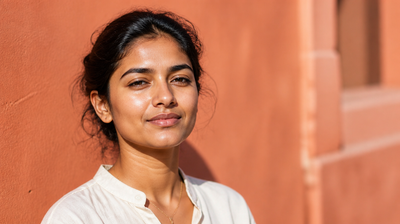 Indian woman outdoors in strong sunlight against a terracotta wall, skin carrying the fresh sheen of just-applied sunscreen