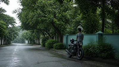 Indian man standing beside his parked motorcycle with his helmet on the seat, on a wet tree-lined monsoon street