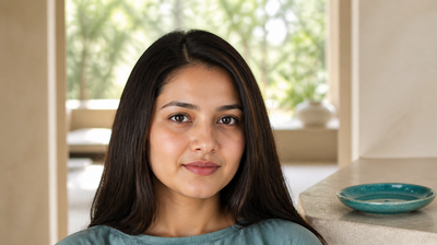 A woman standing in a sunlit room beside a teal glazed ceramic dish, calm after rethinking her exfoliation routine
