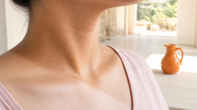 Close view of the side of a woman's neck and collarbone in morning light, showing a soft tan demarcation line where deeper tanned skin meets lighter untanned skin