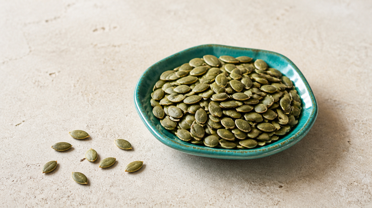 Shelled green pumpkin seeds, a dietary source of zinc, heaped in a teal ceramic dish on pale stone
