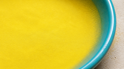 Fine bright yellow sulphur powder filling a turquoise-glazed ceramic dish, shown close up on pale stone