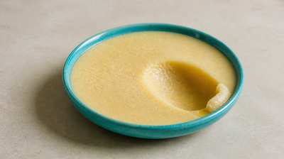 Semi-solid straw-gold ghee in a teal ceramic dish, with a spoon hollow scooped out of its grainy set surface