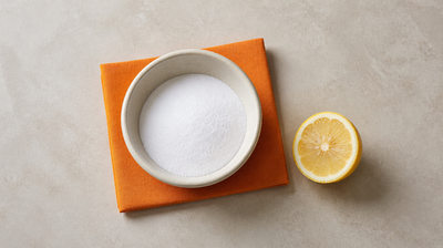 Bowl of white baking soda on orange linen next to a cut lemon half, a common but harsh DIY face remedy