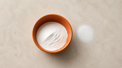 An orange bowl of fine white cornflour with a small spill of powder on pale stone