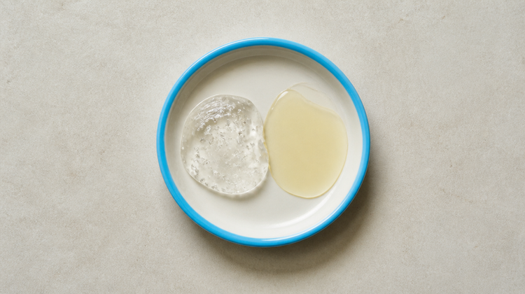 A clear hyaluronic acid gel beside a pale golden vitamin C serum in a blue-rimmed dish, seen from above