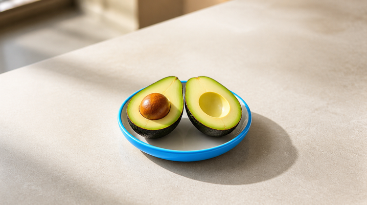 Ripe avocado cut in half, one half with its seed, on a sky-blue saucer, avocado for face