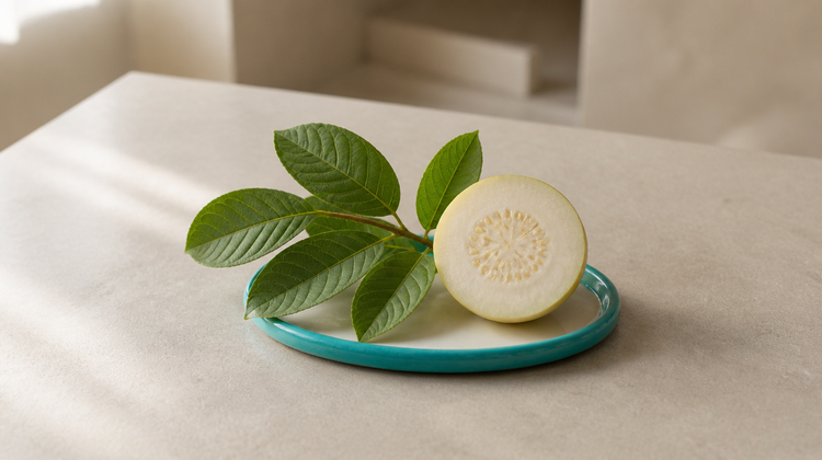 A fresh sprig of ribbed guava leaves and a cut guava on a teal ceramic plate