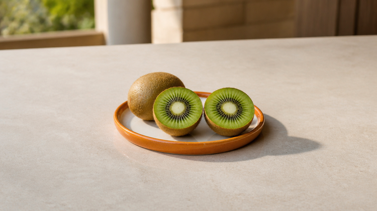 A whole kiwi and a halved kiwi showing green flesh and black seeds on a burnt-orange plate