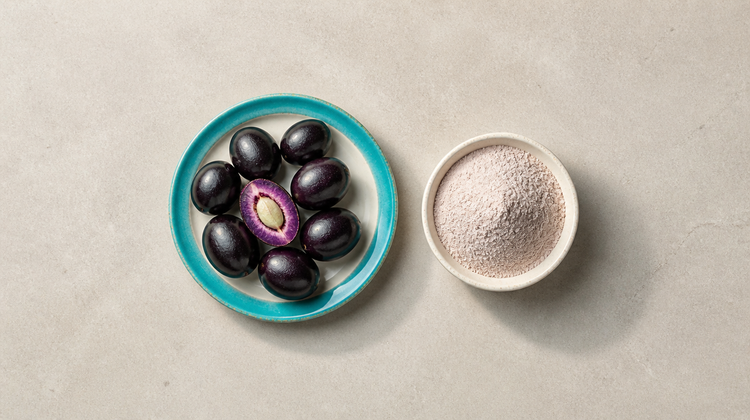 Ripe jamun fruits and a halved jamun showing its seed on a teal plate, beside a bowl of jamun seed powder