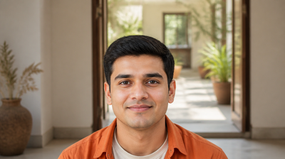 A young Indian delivery rider in a burnt-orange overshirt taking a break in a shaded veranda