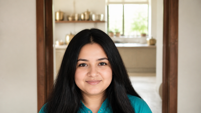 A smiling Indian home cook in a teal kurta standing at the doorway of her sunlit kitchen