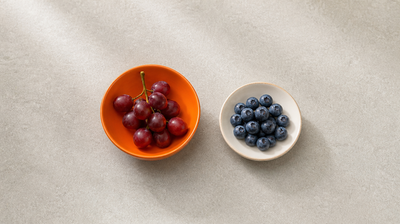 Red grapes in an orange bowl beside a dish of blueberries, natural sources of the antioxidant resveratrol