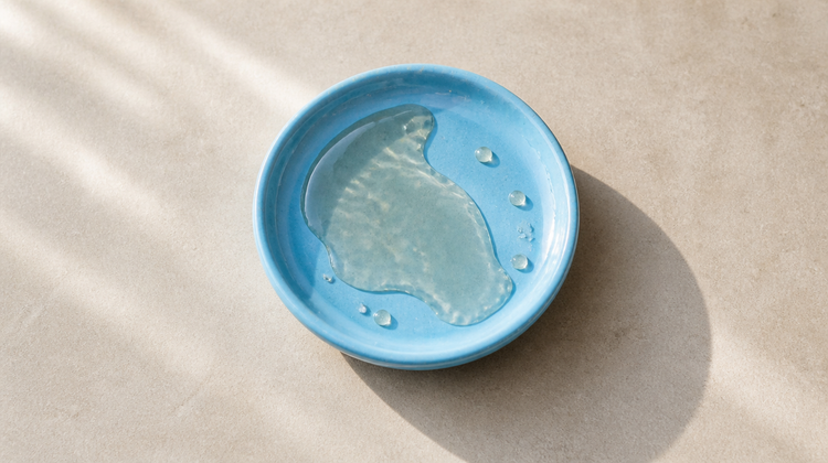 Clear UV-filter oil pooled in a sky-blue ceramic saucer in bright sunlight, illustrating octocrylene in sunscreen
