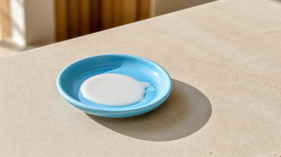 A pool of white sunscreen lotion in a sky-blue ceramic dish in sunlight, for a guide to homosalate in sunscreen