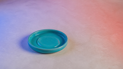 A teal ceramic dish on pale stone washed with soft blue light from one side and red light from the other, the two colours used in LED therapy for acne