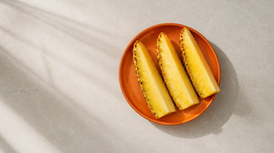 Three fresh pineapple spears with golden flesh and spiky rind on a burnt-orange plate, illustrating pineapple for skin