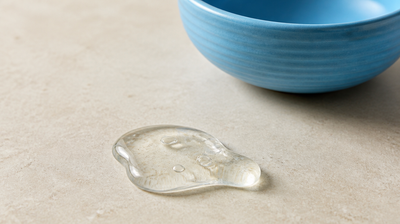 A small blob of clear gel on pale limestone beside a sky-blue stoneware bowl, for an article on adenosine for skin