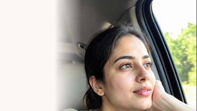 An Indian woman resting her chin on her hand, looking out of a car window in soft daylight