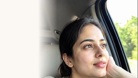 An Indian woman resting her chin on her hand, looking out of a car window in soft daylight