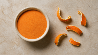 A bowl of fine orange peel powder on honed stone beside curled strips of dried orange peel