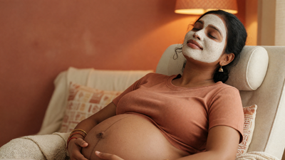 A pregnant Indian woman relaxes in an armchair with a clay face mask on.