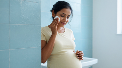 A pregnant Indian woman sweeps a cotton pad across her cheek at the bathroom basin.