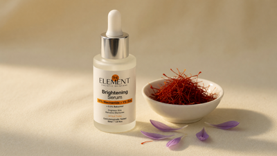 Saffron (kesar) threads in a bowl with crocus petals beside The Element 10% Niacinamide + 1% Zinc Brightening Serum on a cream surface