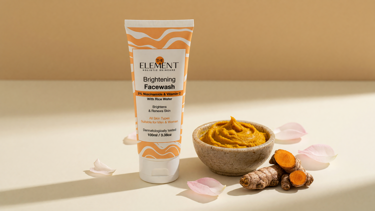A bowl of golden ubtan paste, turmeric roots and rose petals beside The Element Brightening Face Wash with 3% Niacinamide on a cream surface