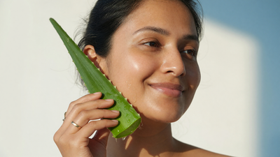Indian woman holding a fresh aloe vera leaf to her glowing, hydrated skin
