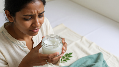 Indian woman holding an open unlabelled jar of coconut oil, considering whether to apply it to her oily, acne-prone face