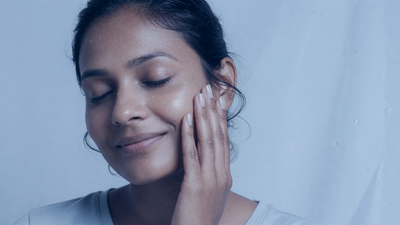 Indian woman with calm, soothed skin resting her fingertips on her cheek