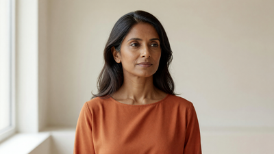 Indian woman in her forties in soft daylight with honest, natural skin texture and fine lines, wearing a terracotta top