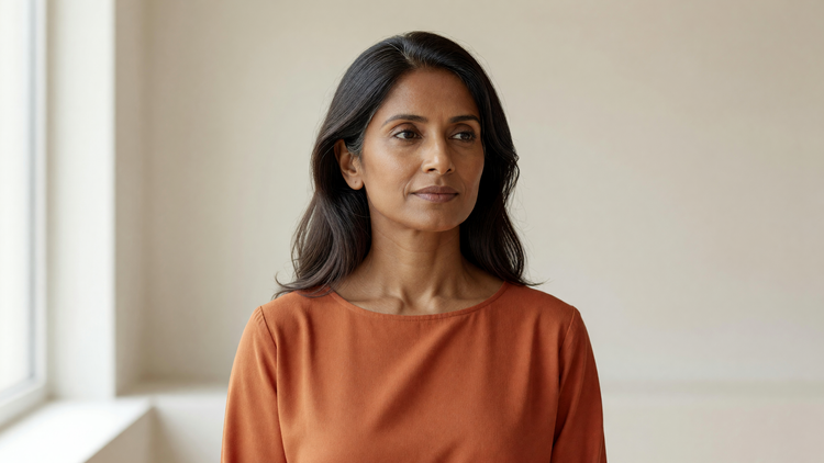 Indian woman in her forties in soft daylight with honest, natural skin texture and fine lines, wearing a terracotta top