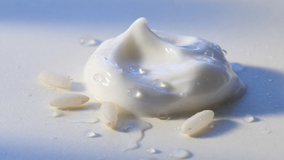 A rich dollop of white moisturiser with rice grains and water droplets — hydration for dry Indian skin with The Element Rice Water Moisturiser.
