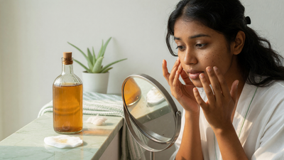 Indian woman examining her skin in a mirror beside a bottle of apple cider vinegar and cotton pads