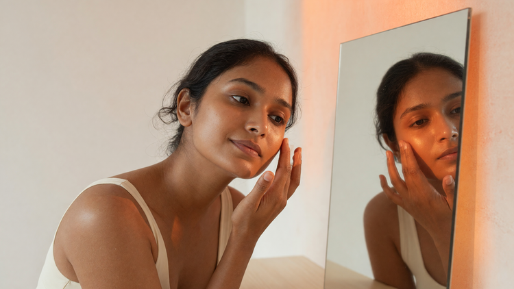 Indian woman with warm brown skin examining her skin type in a mirror