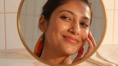 Indian woman with clear, bright, even-toned skin smiling at her reflection in a mirror, illustrating niacinamide results building over time