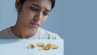 Indian woman looking down at loose amber vitamin E softgel capsules on a white surface, considering whether to apply Evion 400 oil to her face