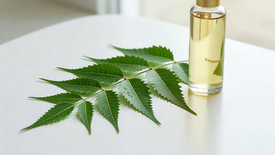 Fresh neem leaves next to a minimalist skincare serum bottle on white surface