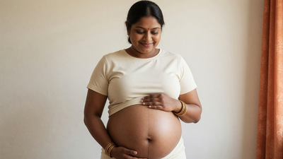 Pregnant Indian woman with warm brown skin cradling her bare bump, a faint linea nigra visible down the midline